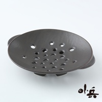 深棕色陶製多用蒸盤，盤面佈滿大小不一的透氣孔，盤緣有兩個小提把，盤底有三個支撐腳。