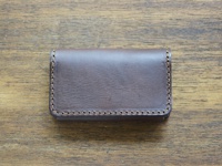 深棕色皮革製成的職人手作Organ名片夾，以咖啡色車線縫合邊緣，置於木紋桌面。