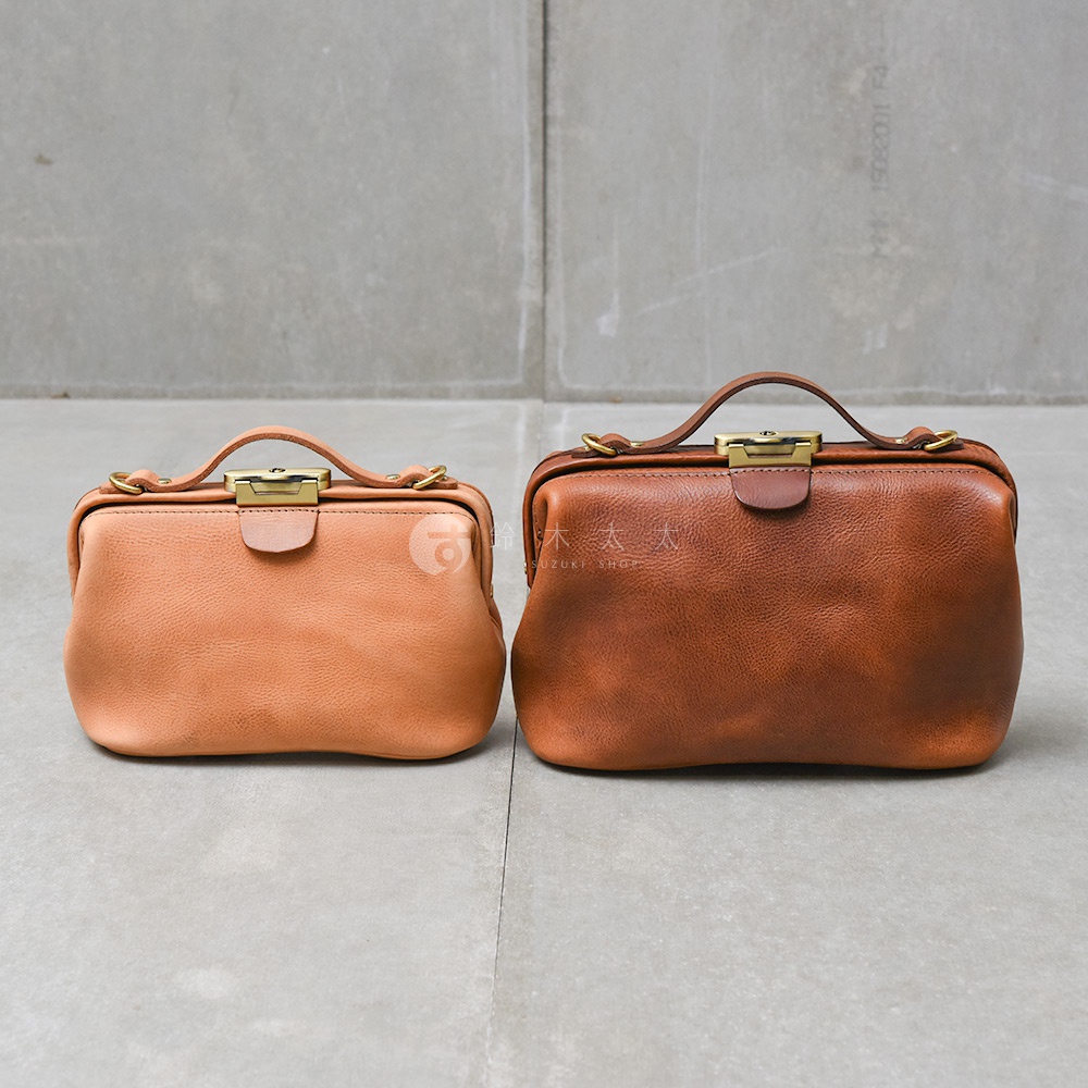 兩個日本HERZ職人手作皮革Organ鎖孔式大開口肩背包，一個淺棕色，一個深棕色，並排置於灰色水泥地上。