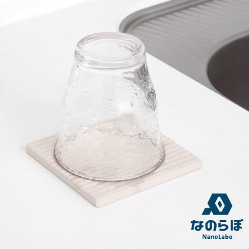 一個透明玻璃杯倒置在一個淺米色、帶有細微紋理的方形珪藻土置物墊上。置物墊放置在白色檯面上，背景是水槽的灰色邊緣。