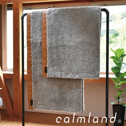 兩塊灰色毛圈織物廚房地墊，其中一塊飾有皮革飾邊，懸掛在黑色金屬架上。