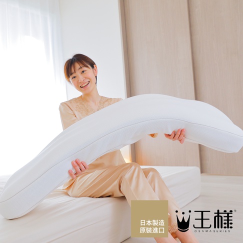 一名女子坐在床上，雙手捧著一個白色、長條形、彎曲的枕頭，枕頭表面有細密的網狀紋理。