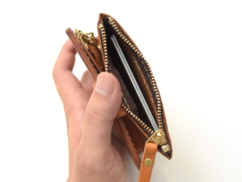 手持棕色皮革拉鍊零錢鑰匙包，露出內部夾層，展示有六個鑰匙鉤和卡片。