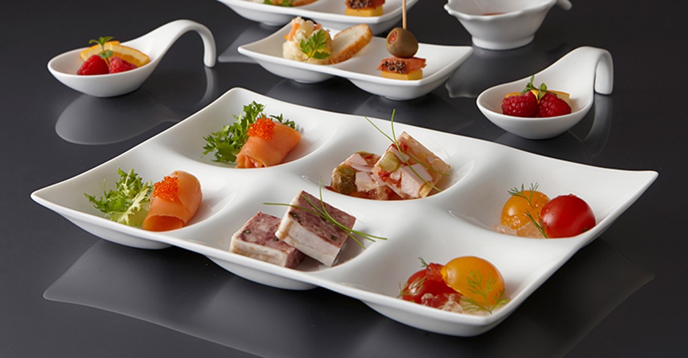 白色陶瓷三格小菜盤，盛裝著鮭魚捲、肉凍、火腿塊及小番茄等精緻開胃菜，盤身線條流暢，風格簡約。