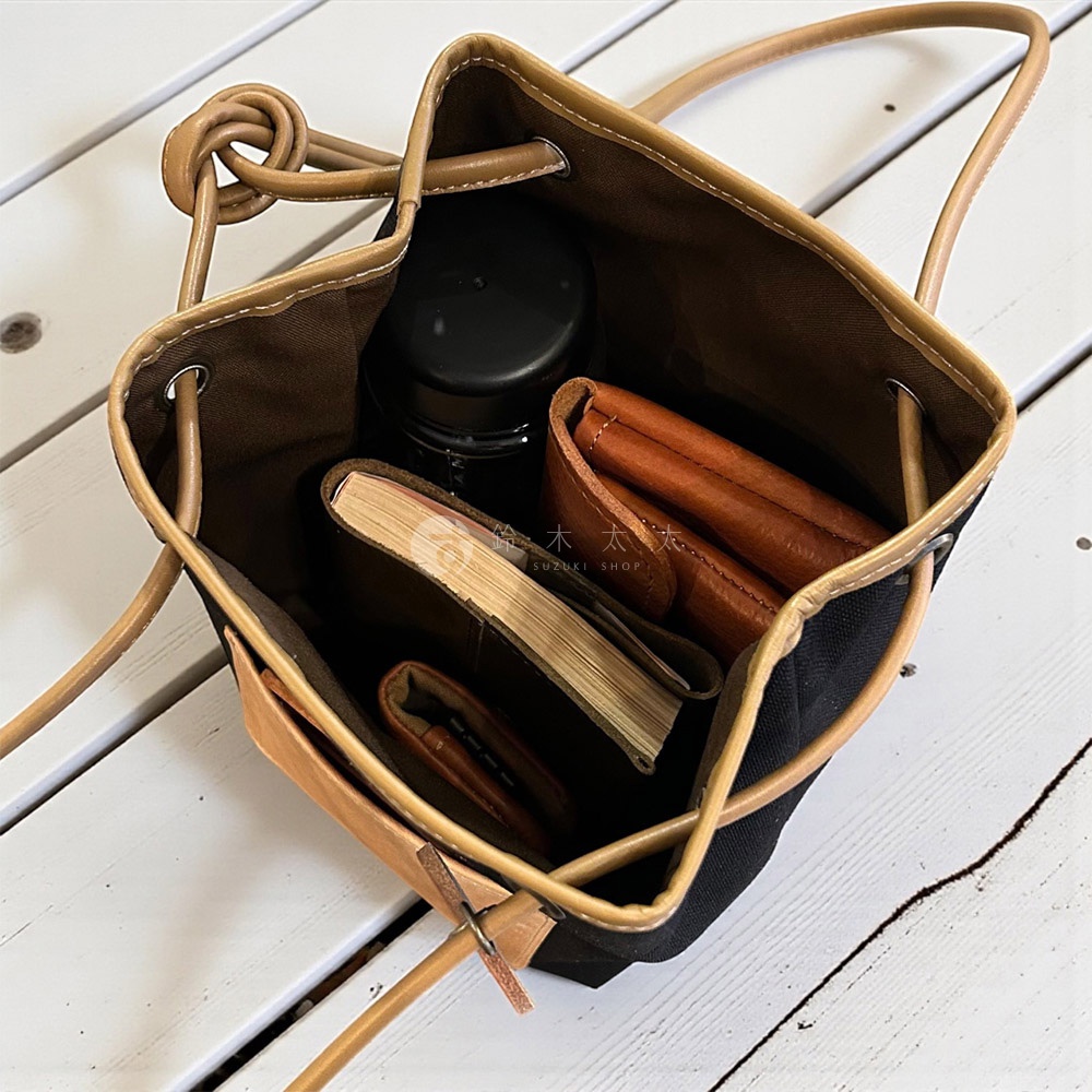 神戶clueto nico 防潑水尼龍 x 義大利皮革束口肩背包，包內有書籍、錢包和水瓶