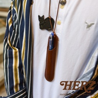 HERZ Handmade in Japan Since 1973，一個棕色皮革筆套掛在白色POLO衫上，筆套內有藍色筆，筆套上方有一個黑色貓咪造型墜飾。