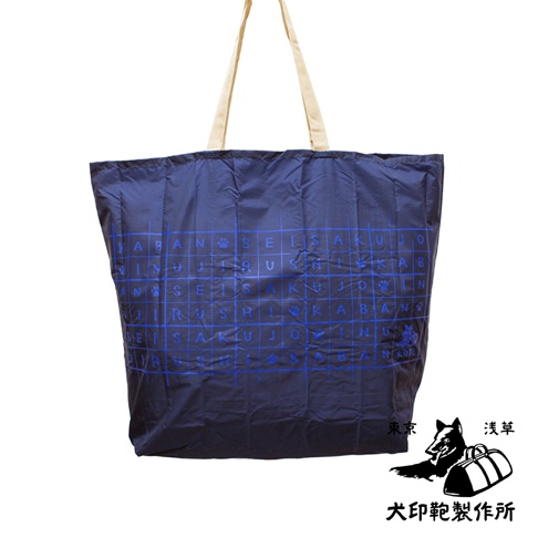 深藍色環保折疊收納購物袋，布料材質，袋身印有藍色網格及日文文字與狗爪圖案，配有米色織帶提把。