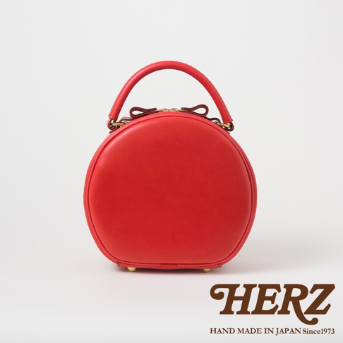 日本HERZ品牌紅色皮革手提圓形包，配有金色扣環和蝴蝶結裝飾，下方印有HERZ品牌標誌和「HAND MADE IN JAPAN Since1973」字樣。
