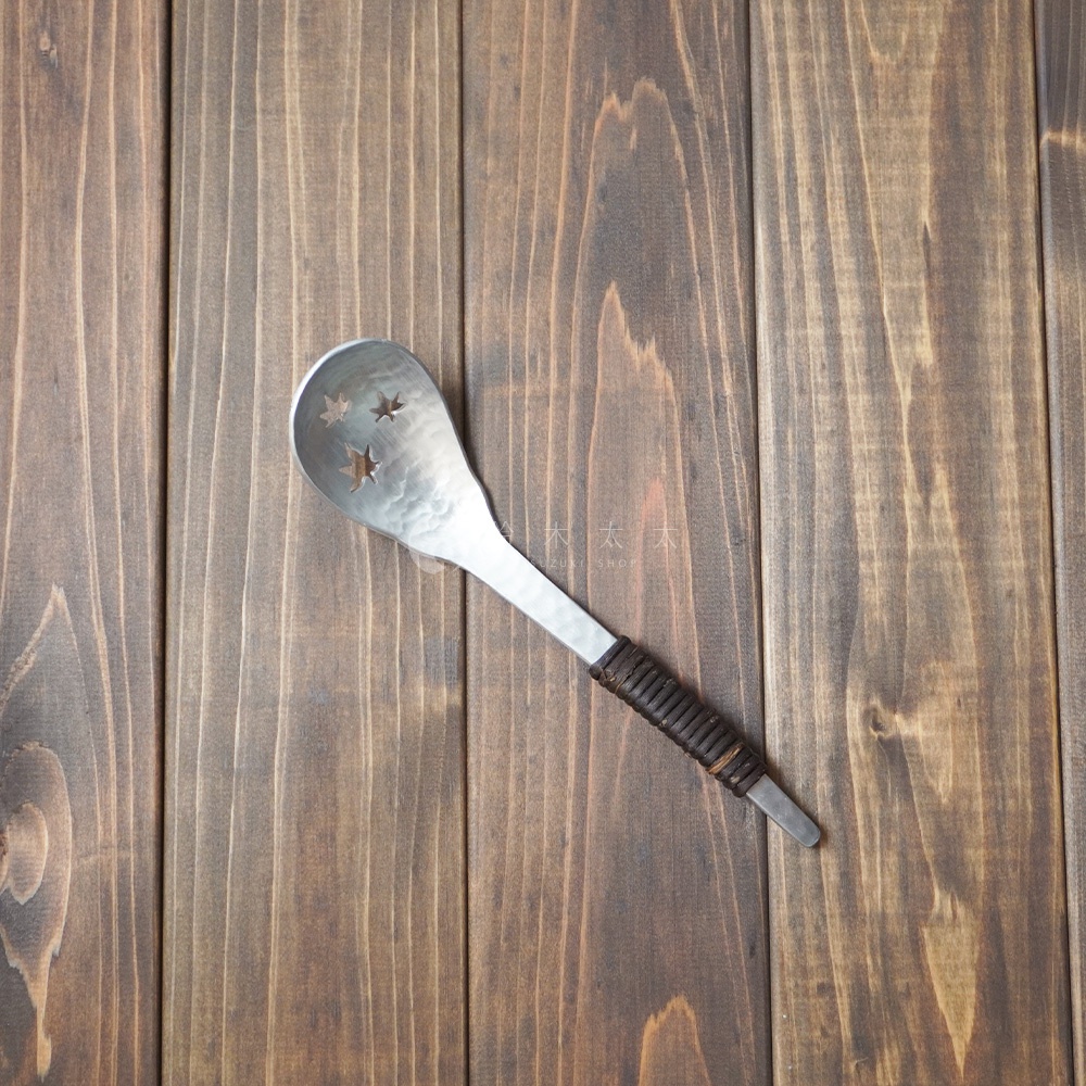 一個帶有錘目紋和三顆星形鏤空設計的銀色鋁製瀝水湯勺，勺柄處纏繞著深棕色皮革。