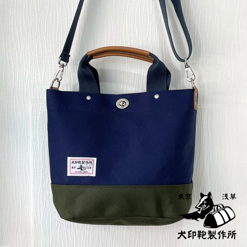 海軍藍與墨綠色拼接的純棉帆布兩用托特包，配有棕色皮革提把與可拆卸肩帶。包身有品牌標籤與金屬旋轉扣。