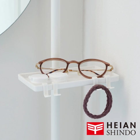 白色塑膠置物托盤，上面放置一副棕色鏡框的眼鏡、兩個白色瓶蓋，以及一個紫色髮圈。托盤下方有白色掛鉤。