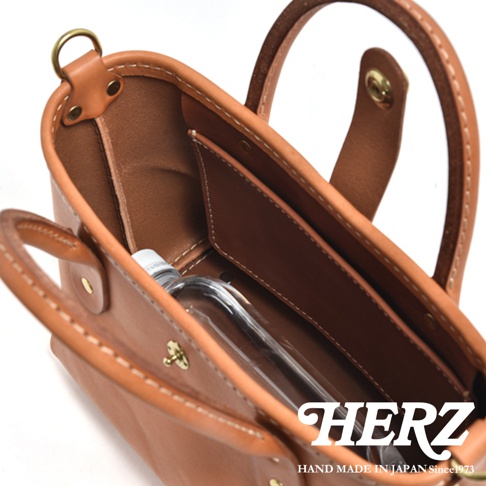 職人手作皮革迷你托特包，淺棕色牛皮材質，內部有隔層，可見一瓶透明水瓶。