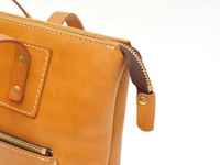 職人手作皮革威靈頓直式拉鍊托特包 (T-151) 的特寫，展示了淺棕色皮革材質、黃銅色拉鍊及縫線細節。