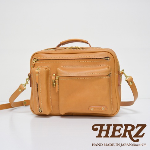 職人手作皮革兩用多功能收納單肩包，淺棕色皮革材質，正面有兩個拉鍊隔層、一個翻蓋口袋及一個直向拉鍊口袋，配有可拆卸肩帶及手提把。