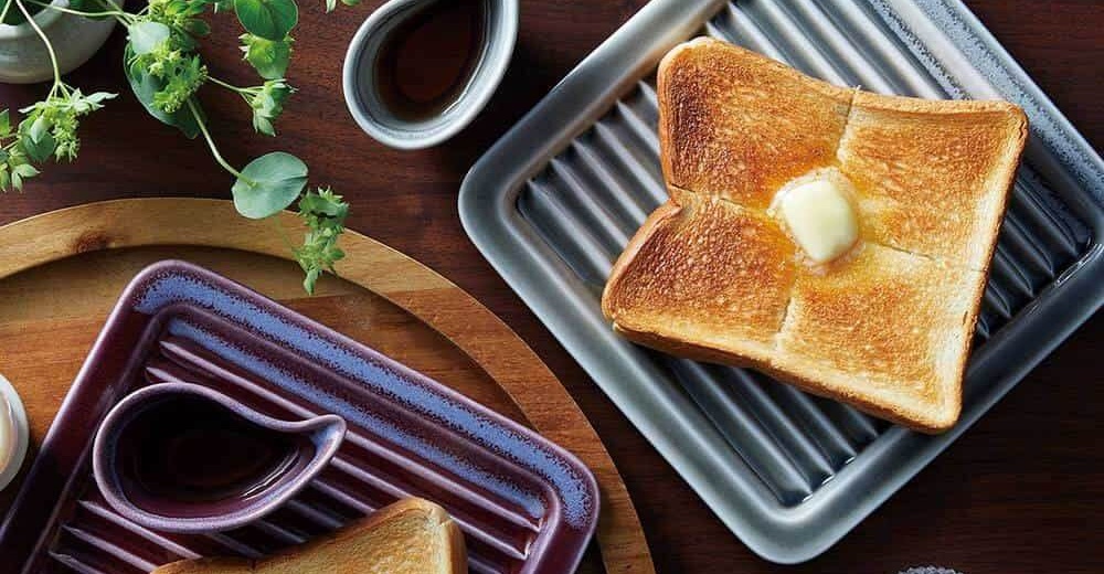 左側為紫羅蘭色美濃燒素釉吐司酥脆專用盤，帶有條紋和醬料碟；右側為銀灰色美濃燒素釉吐司酥脆專用盤，盤上放著一片塗有奶油的烤吐司。