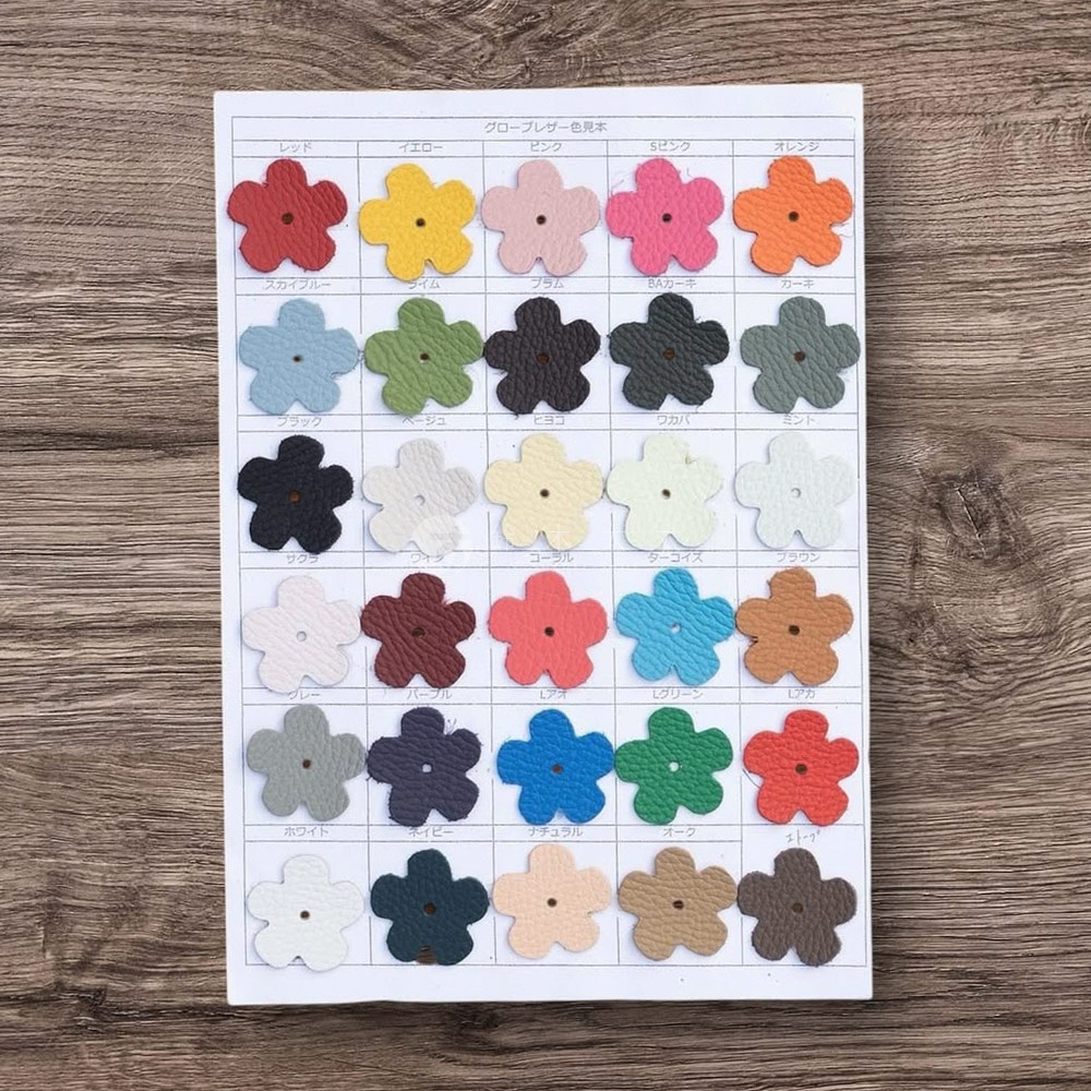 這張圖展示了京都職人手作多功能收納包的皮革色卡，共五列，每列五行，共二十五種顏色。每個顏色樣品都是五瓣花朵形狀，材質為皮革。顏色包含紅色、黃色、粉色、S粉色、橘色、天空藍、萊姆綠、普拉姆紫、BA卡其綠、卡其綠、黑色、米色、淺黃色、淺綠色、淺藍色、櫻花粉、米白色、勃艮第紅、珊瑚紅、藍綠色、淺棕色、淺灰色、海軍藍、皇家藍、綠色、紅色、象牙白、淺棕色、淺米色、棕色。