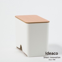 白色塑膠製成的口罩收納抽取盒，頂部覆蓋著淺木色原木蓋，盒身側面下方有彎曲的開口設計。