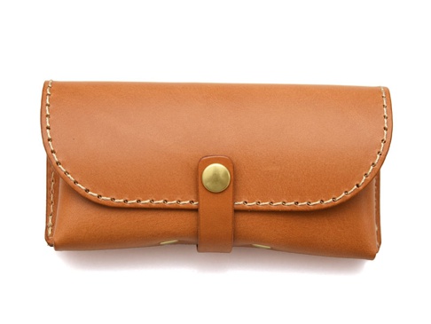 職人手作皮革眼鏡收納盒，採用棕褐色皮革製成，帶有金屬釦帶，邊緣以白色縫線裝飾，設計簡約。