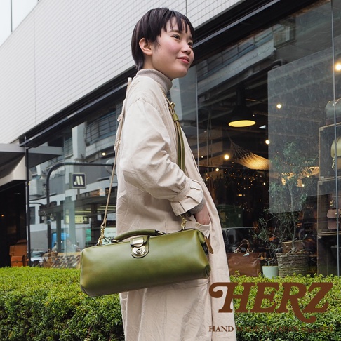 日本HERZ職人手作綠色皮革橫長形杜勒斯單肩包，一位女性斜背著包包，包包上有金屬鎖扣。