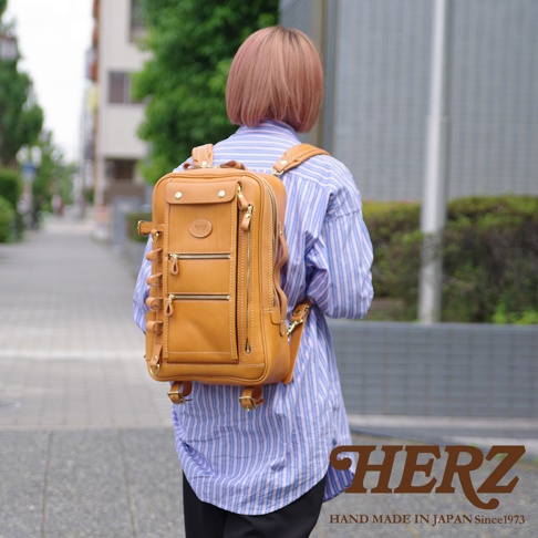 一位女士背著棕褐色皮革製成的兩用多功能後背包，背包上有兩個拉鍊隔層和一個頂部翻蓋口袋，側面有可調節的皮革帶。