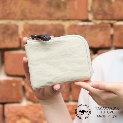 TUTUMU 品牌米白色防潑水迷你錢包，以手指托住，背景為磚牆。