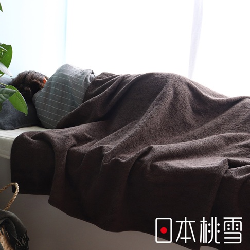 一條深棕色的雙面毛圈長棉毛巾被，覆蓋在一位睡著的人身上，毛巾被材質柔軟，呈現自然的褶皺。