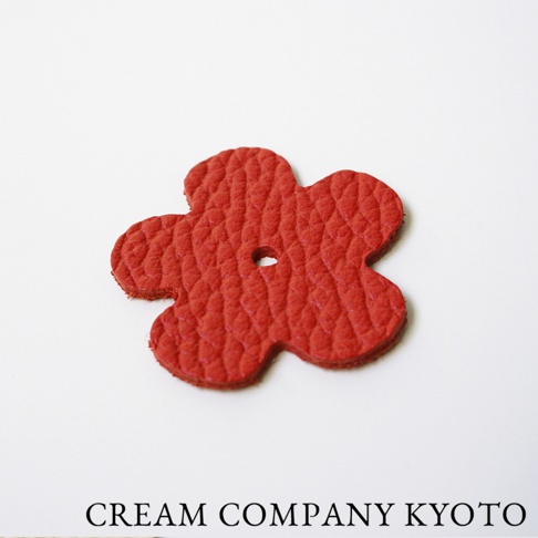 紅色皮革製成的五瓣花形狀吊飾，表面有紋理，中央有一個小圓孔。