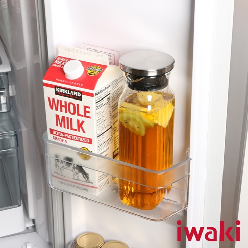 透明耐熱玻璃水壺，內含琥珀色液體及水果切片，搭配不鏽鋼蓋，置於冰箱層架上。