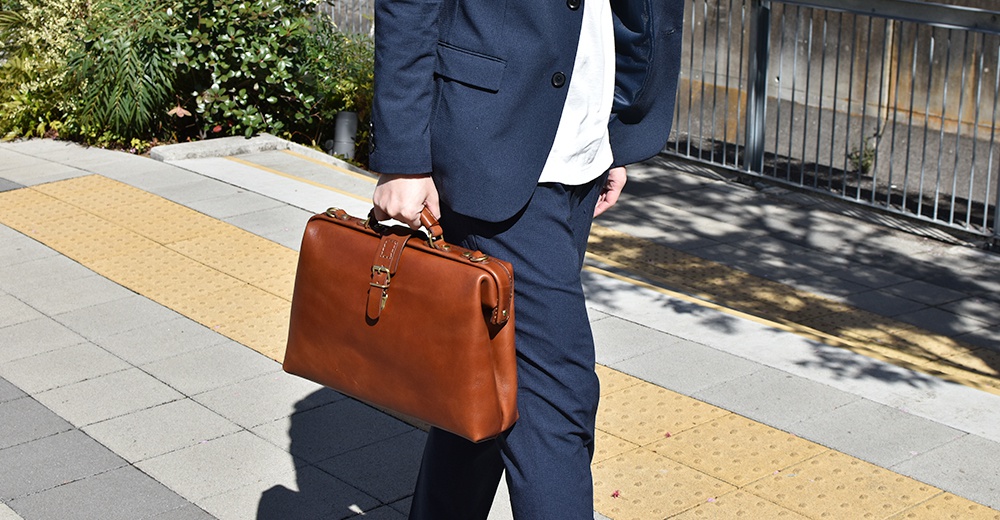 職人手作皮革軟式杜勒斯包，經典棕色，帶有金屬釦環和提把，適合商務用途。