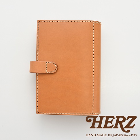職人手作淺棕色皮革記事本書套，圓形皮革鈕扣開合，車縫線明顯，簡約設計。