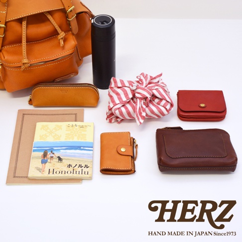 職人手作皮革復古風旅行後背包 R-65，包含一個橘棕色皮革後背包、一個橘色筆袋、一個黑色保溫瓶、一條紅白色條紋布包、一個紅色皮夾、一本 Honolulu 圖書、一個橘色皮夾和一個深棕色皮夾。