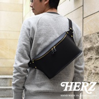 黑色皮革立體斜背包，搭配金色拉鍊與釦環，由日本HERZ品牌手工製作，展現職人技藝。