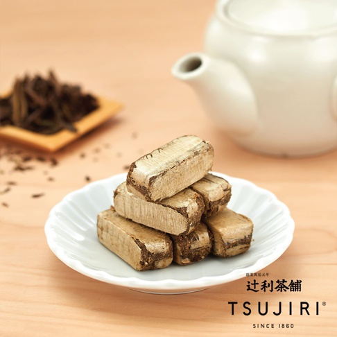 淺色木紋背景上，一個白色波浪邊緣小碟堆疊著幾塊長方體茶酥，旁邊擺放著一小堆深色茶葉與一個白色茶壺，右下方標示著辻利茶舖品牌名稱與創立年份。