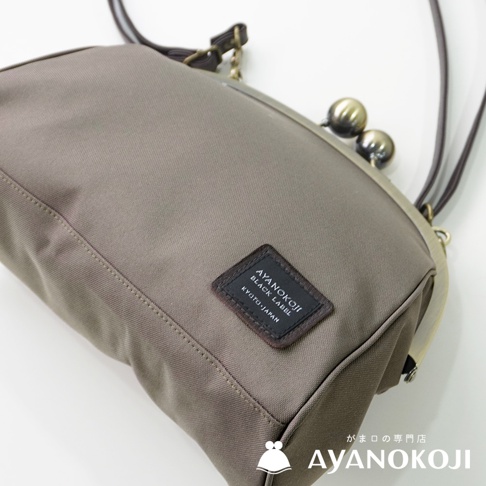 一個灰褐色的綾小路京都職人手作斜背包，特寫其古銅色口金與標籤，此為視角特寫