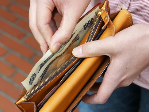 雙手正在打開一個棕褐色皮革長夾，夾內有日圓鈔票和卡片，以及一個深棕色拉鍊。