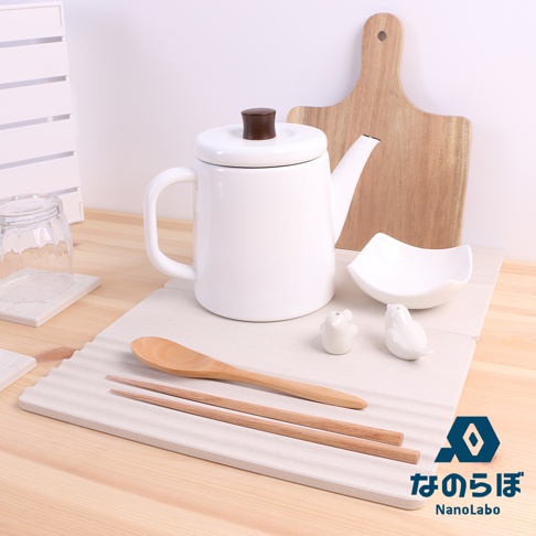 淺灰色珪藻土置物墊上擺放著白色帶咖啡色壺蓋的茶壺、木質湯匙、兩雙木筷、白色小鳥造型擺飾、白色小碗，以及一個木質砧板。