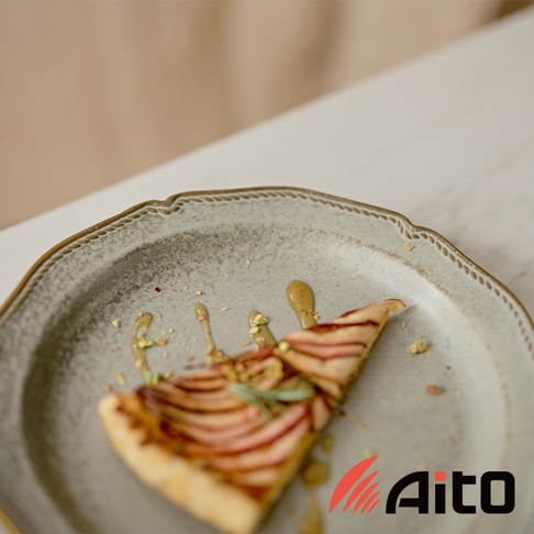 Aito 金彩浮雕經典餐盤上擺放著一片淋有醬汁和開心果碎的蘋果派
