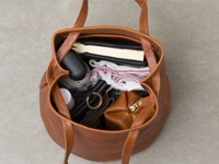 棕色皮革托特包，包內裝有筆記本、折疊傘、化妝品及其他個人物品，包的正面有一個金屬拉鍊。