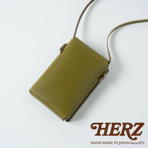 橄欖綠皮革製成的手機包，附有細長背帶，包身簡約，呈現職人手作質感。