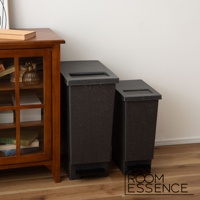 兩個黑色附蓋簡約垃圾桶，其中較大的一個有腳踏板，置於木櫃旁。