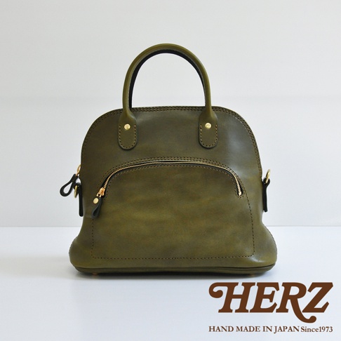 橄欖綠皮革手提包，經典貝殼造型，設有頂部提把、金色拉鍊前袋與側邊掛環。