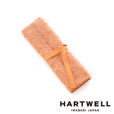 一條捲起的橘色毛巾，以同色系的織帶固定，毛巾材質為柔軟吸水的今治毛巾布。