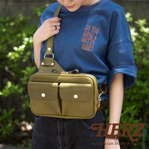 橄欖綠皮革雙口袋斜背包，配有金色金屬鈕扣和拉鍊，質感皮革材質，簡約實用設計。