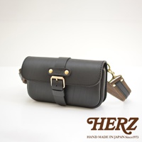 黑色皮革材質的單扣斜背包，正面有品牌標誌和金屬扣環，附有可調節的織帶和皮革肩帶，整體設計簡約經典。