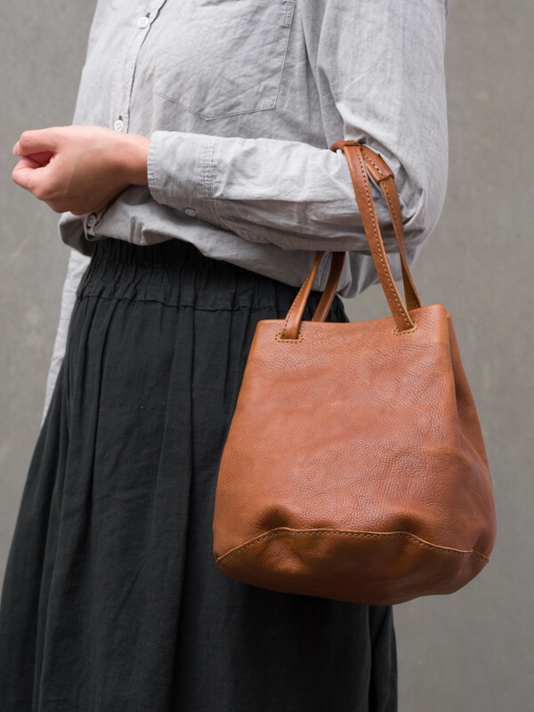 棕色皮革抽繩水桶包，配有兩條短提把，可肩背或手提。包身材質柔軟，底部有縫線設計。