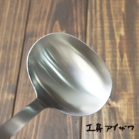 一個銀色不鏽鋼萬用湯勺，勺面寬大，手柄部分可見，背景為木紋桌面。