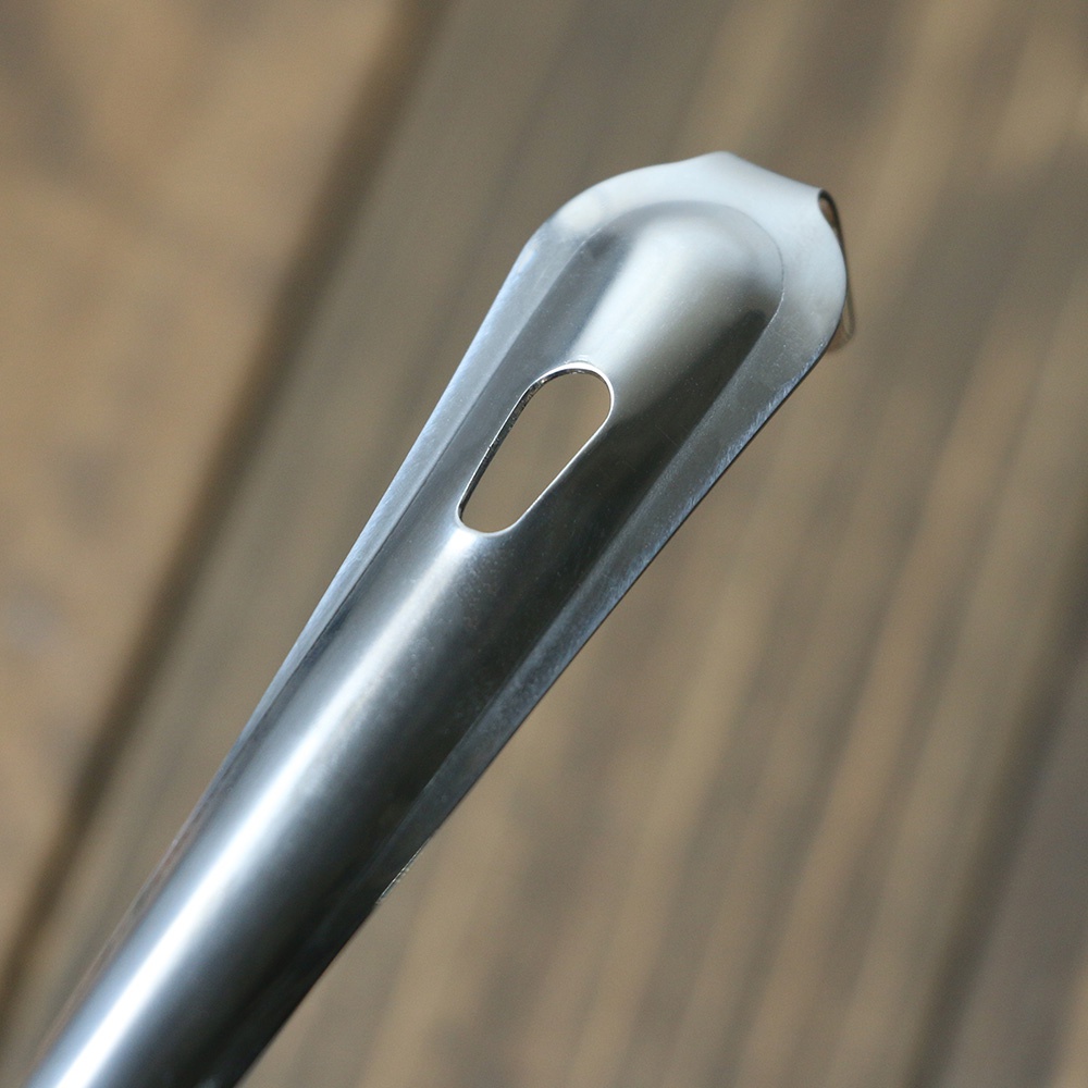 不鏽鋼中型撈勺的特寫，勺身呈銀色金屬光澤，帶有一個橢圓形的漏孔，勺邊緣光滑，背景為模糊的木紋。