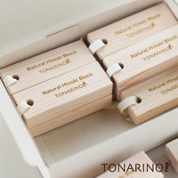 一盒裝有16個淺色天然檜木條，每個檜木條上都印有金色字體「Natural Hinoki Block TONARINO」及圖案，並以白色緞帶繫住。