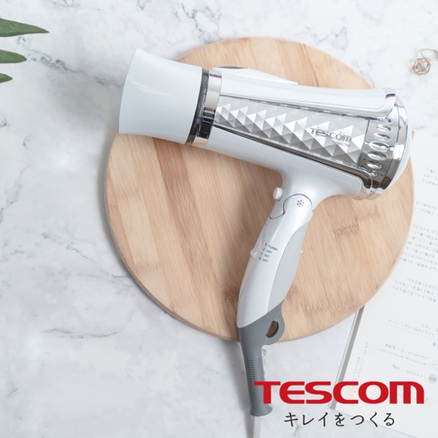 TESCOM 品牌白色負離子吹風機，機身飾有菱形紋路，置於木質圓盤上，背景為大理石紋路。