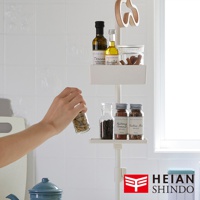 白色直撐款置物架，上面層架擺放兩瓶橄欖油、一瓶肉桂粉和一瓶綜合香料，下方層架有兩瓶香料，左手持一瓶綠色香料。